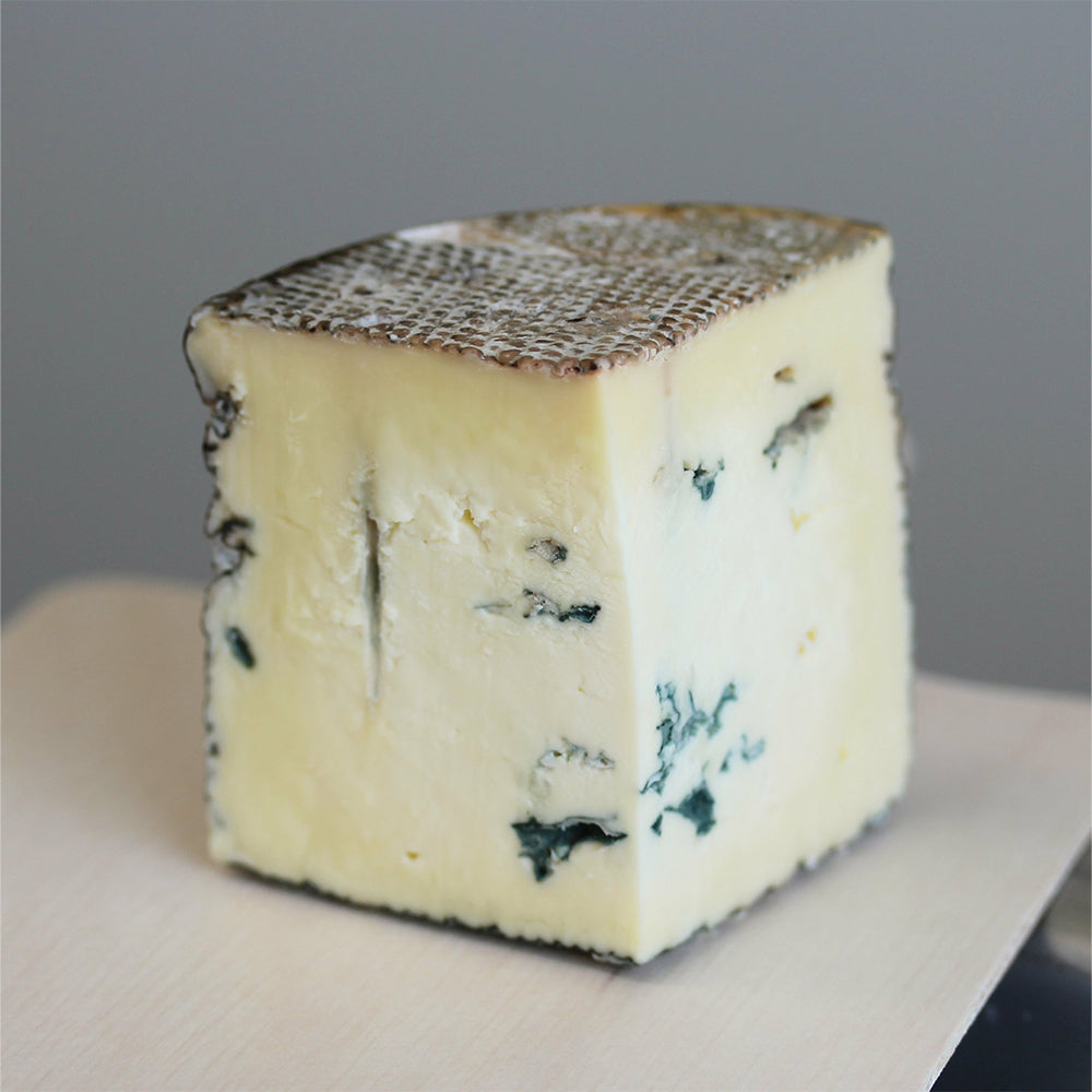 A quarter-wheel wedge of Lost Lake Blue, a creamy farmstead blue cheese, showing its rich blue veining and soft texture.