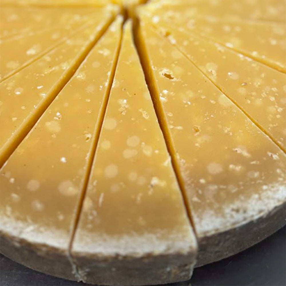 A wedge of Alparm, a 2-year aged farmstead alpine cheese, showing its golden rind and firm, crystalline interior.