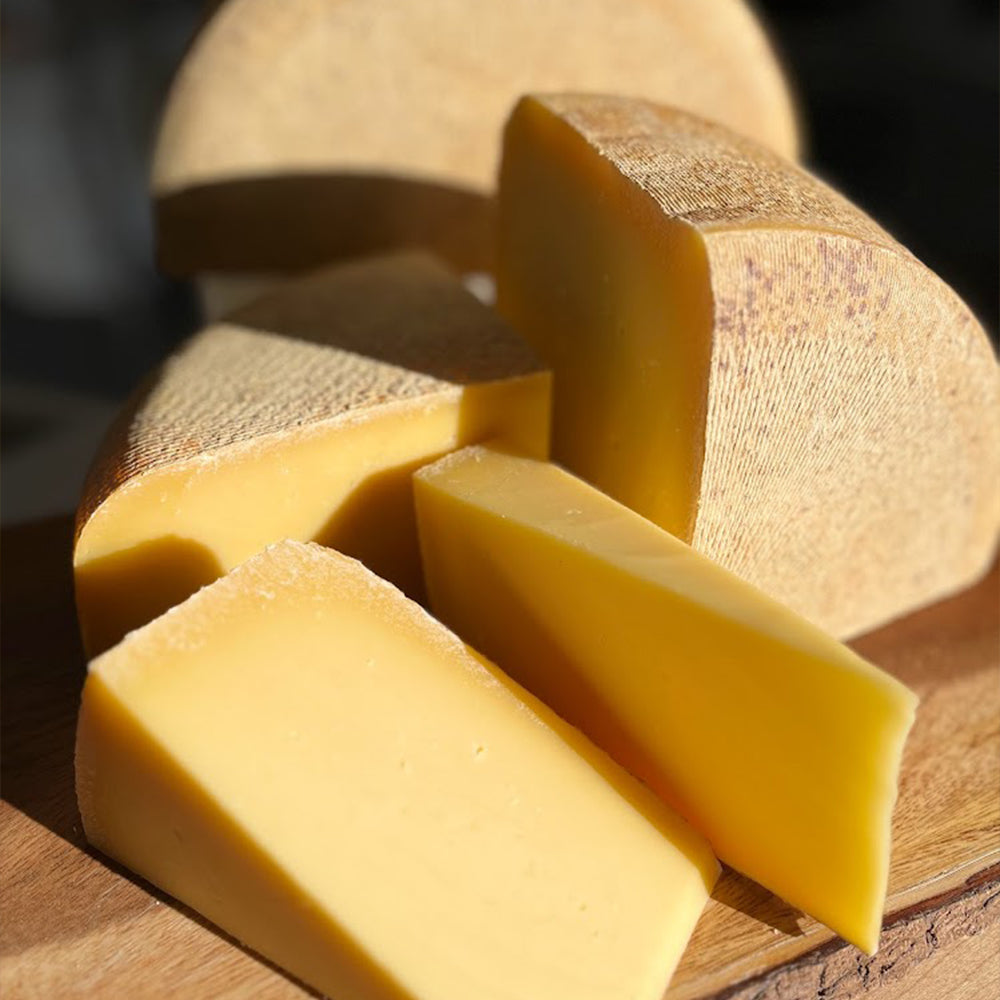 Slices of sharp, aged Iowa Alpine (a Gruyere style cheese) served on a cheeseboard with crackers and jam.